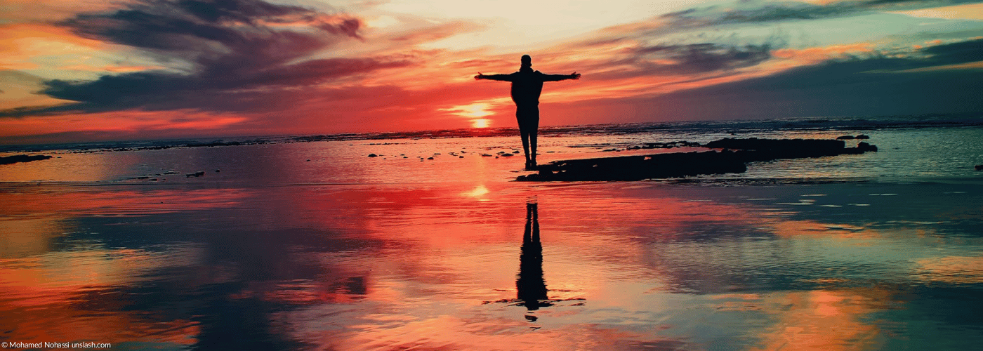 Mensch mit ausgestreckten Armen im Sonnenuntergang am Meer